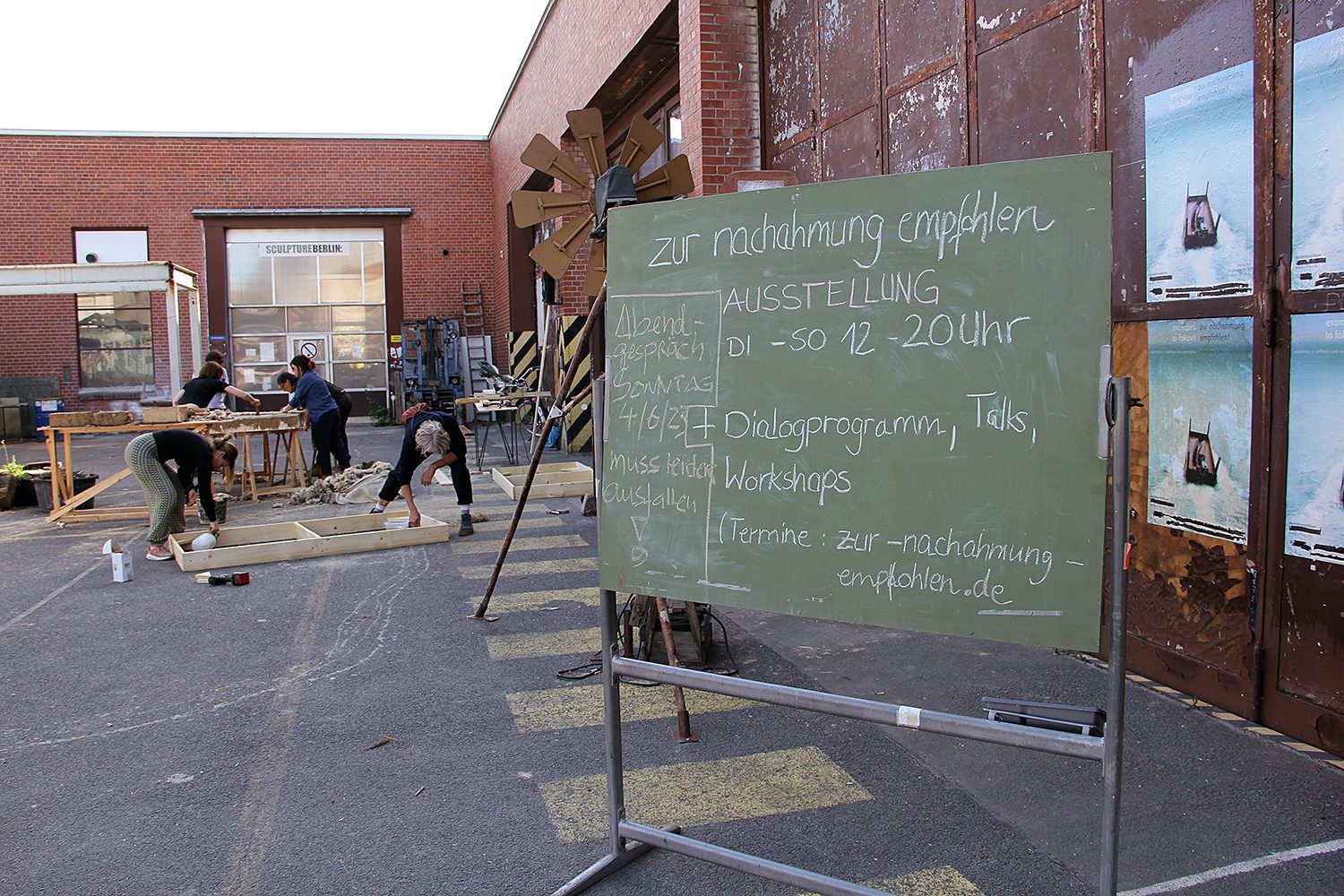 Die Tafel weist auf die Ausstellung "ZNE -Zur Nachahmung empfohlen" und das Rahmenprogramm in den Uferhallen hin. Im Hintergrund arbeiten Künstler an einem der Kunstwerke. Foto: Hensel