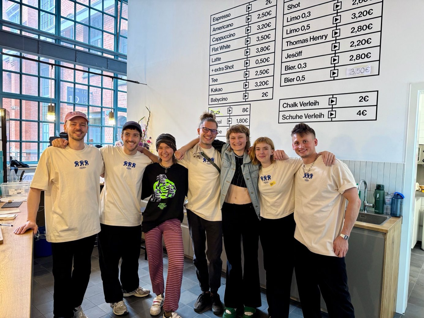 Das Team der Boulderhalle "Das Elektra" steht lächelnd Arm in Arm im Eingangsbereich.