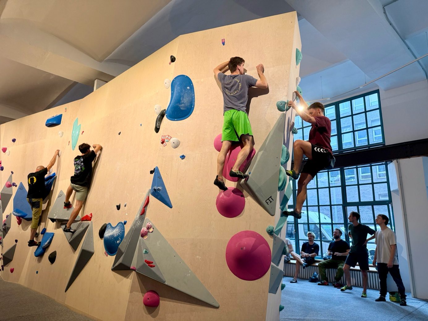 "Das Elektra" Boulderhalle - Wände mit bunten Bouldern, Menschen bouldern an der Wand und stehen am Rand und sehen zu.